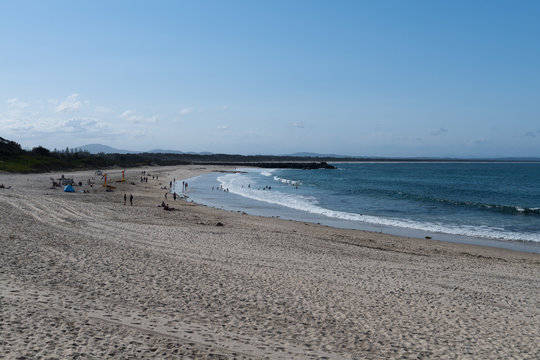 Badenstrand mit weitläufiger Sandfläche im Vordergrund und Badegästen im hinteren Bildteil