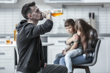 Man drinking alcohol while wife hugging their son on background - obrazy, fototapety, plakaty