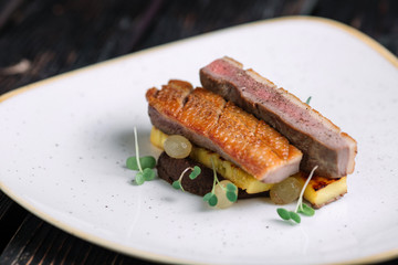 Duck fillet with polenta on irregular shape plate on dark wood background