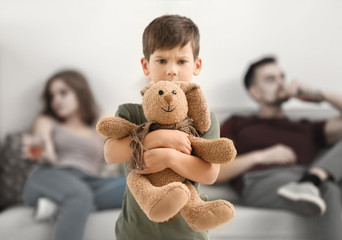 Upset little boy hugging toy bunny while his parents drinking alcohol on background