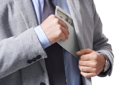 Man in formal suit putting envelope with bribe in pocket on white background, closeup
