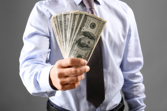 Man in formal clothes holding money on grey background