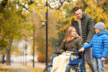 Teenage girl in wheelchair with her family outdoors on autumn day