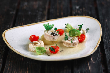 Rolled herring with vegetable on irregular shape plate on dark wood background