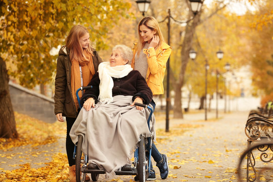 Elderly woman in wheelchair with her family outdoors on autumn day
