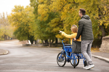 Man with his wife in wheelchair outdoors on autumn day