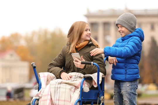 Teenage girl in wheelchair with her brother outdoors on autumn day