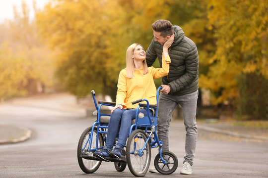 Man with his wife in wheelchair outdoors on autumn day
