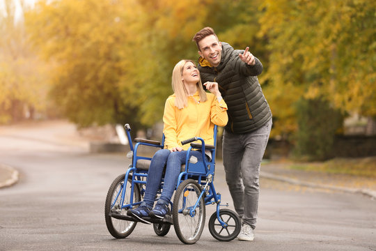 Man with his wife in wheelchair outdoors on autumn day