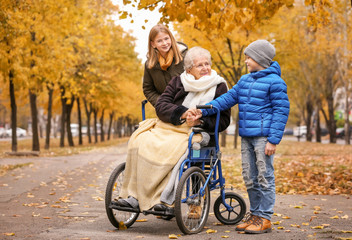 Fototapeta na wymiar Cute children with their elderly grandmother in wheelchair outdoors on autumn day