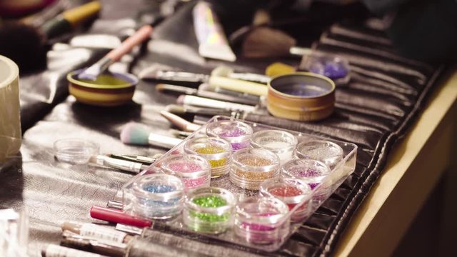 Close up. Jars with colorful shiny powder for art make-up and make-up brushes laying on the table