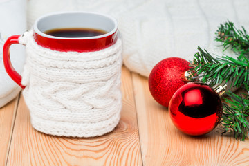 a branch of Christmas fir, red balls and a cup of tea in a knitted sweater on a wooden table