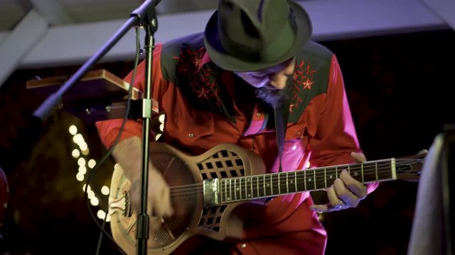Closeup of resonator guitarist as he jams to the music at an outdoor garden restaurant.