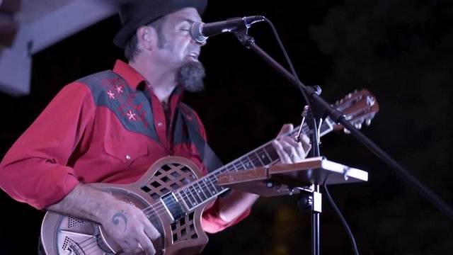 Closeup of guitarist playing a resonator at a live performance outside at night.