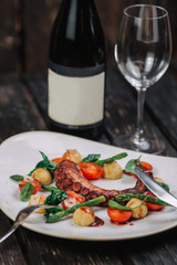 Fried octopus tentacles with wineglass and bottle of wine on white plate on dark wood background