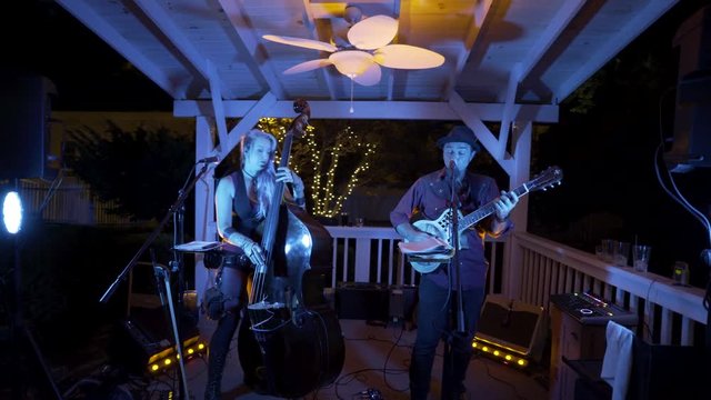 Orbit of blues band playing and singing outside in a garden under a gazebo with blue lights on them.