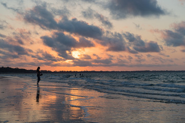 Fototapeta premium Einzelne Frau beim Spaziergang am Strand während Sonnenuntergang blickt aufs Meer