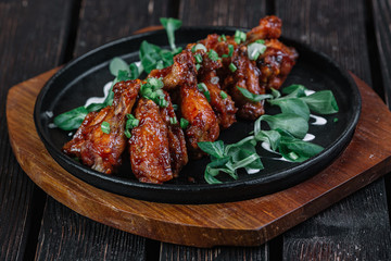Frying pan of chicken wings on the cutting board on dark wood background