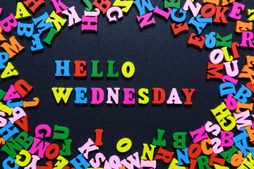 concept design - the word HELLO WEDNESDAY from multi-colored wooden letters on a black background, creative idea
