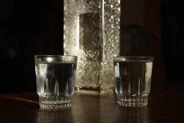 two glasses of vodka and a bottle stand on a table on a dark background