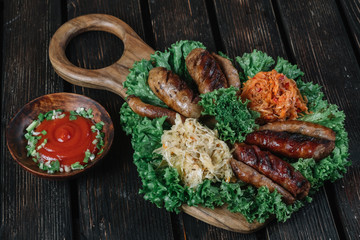 Different kinds of grilled fried sausages with stewed cabbage and sauerkraut. Snacks for beer on dark wood background.