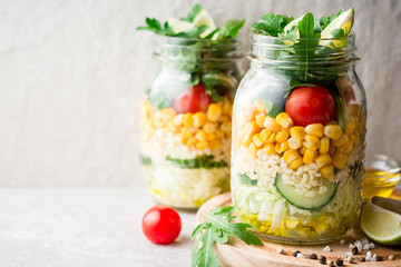 Healthy homemade salads with bulgur, vegetables and lime in mason jars on grey stone background.