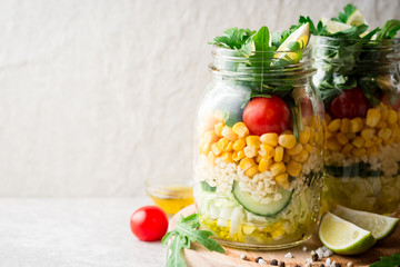 Healthy homemade salads with bulgur, vegetables and lime in mason jars on grey stone background.