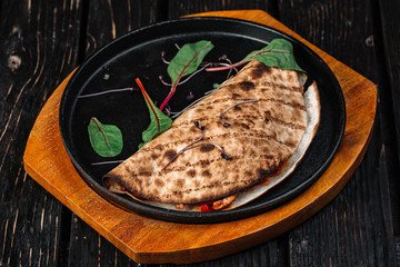 Pita wrapped with meat on the frying pan on dark wood background