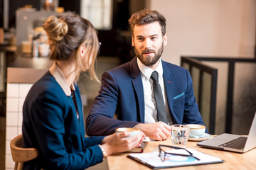 Conversation between business couple dressed in suits sitting with coffee and laptop at the cafe or restaurant