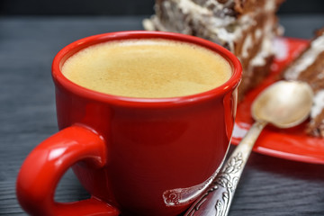 sour cream cake with cream and fresh coffee in a red mug on a dark wooden background