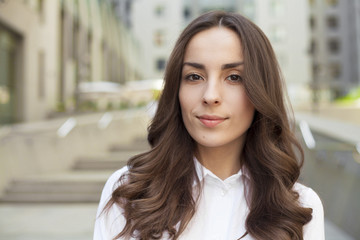 Portrait of a confident modern business woman with beautiful lush hair on the background of an office center in the city and looks on camera.