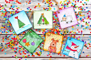 New Year (Christmas) cards with funny snowman, christmas tree, dog, lamb on white wooden background with multicolored confetti . Top view. Merry christmas and happy new year greeting card