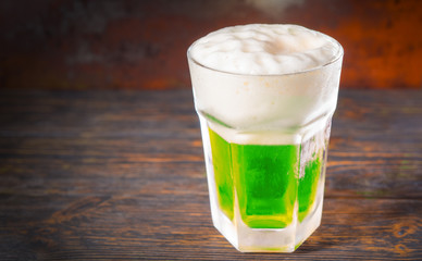 Frozen glass with a green beer and a large head of foam on old dark desk
