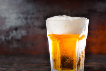 Big glass with a light beer and a head of foam on old dark desk