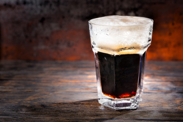 Big glass with freshly poured dark beer and head of foam on wooden desk