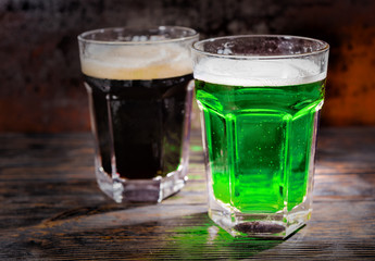 Two big glasses with freshly poured dark and green beer on wooden desk