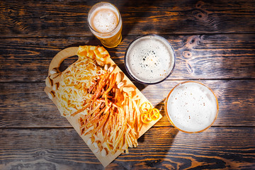 Top view of a lot of different tasty dried fish and squid as beer snacks on wooden cutting board near beer glasses