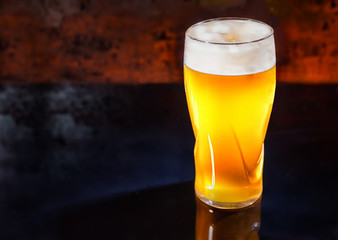 Glass with freshly poured unfiltered light beer on a black mirror surface