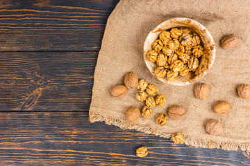 Top view of slightly scattered walnuts lying on linen cloth near wooden plate with walnuts on wooden desk