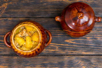 Top view of clay pots with hot roast potatoes with cheese and spices on a wooden desk