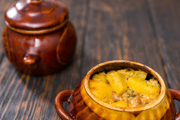 Roast potatoes, cheese and spices in a clay pot on a wooden desk