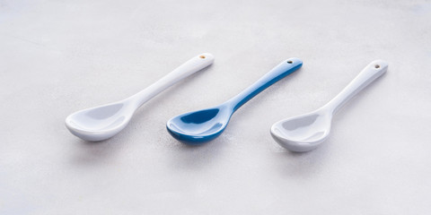 Three empty spoons with one different color in the middle on gray background. Diversity choice concept