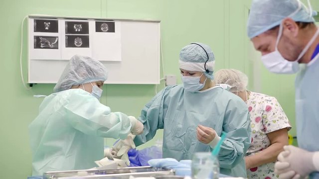 surgeon woman is preparing for operation, she is standing in a light hall, nurses are helping her to wear