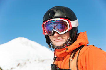 Portrait of a skier in an orange overall with a backpack on his back in a helmet stands against the background of a beautiful Caucasian mountain landscape