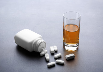 Glass of alcohol and bottle with pills on grey background