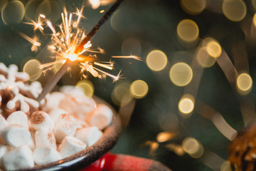 Obraz na płótnie Canvas Close view of marshmallow in red cup with sparkler. soft selective focus. abstract bokeh background, copy space. Christmas or New Year composition.