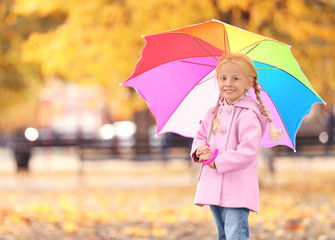 Obraz premium Cute little girl with rainbow umbrella in autumn park