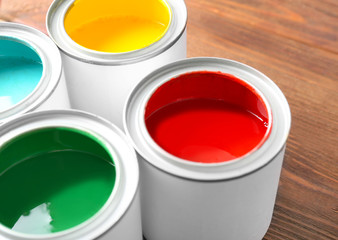 Multicolored paint in tin cans on wooden background, closeup