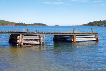 Fototapeta na wymiar Wooden bridge in the blue sea, islets in the Finish archipelago in the background