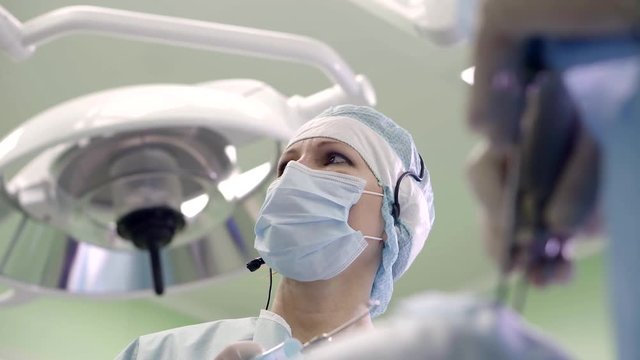 woman surgeon is wearing mask, hat and headset is standing in operation room during endoscopic procedures